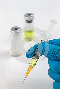 Gloved hand holding a syringe with vaccine bottle on background