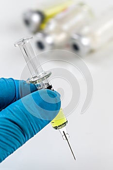 Gloved hand holding a syringe with vaccine bottle on background