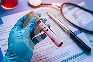Gloved hand holds DNA TEST tube with red liquid in medical lab.