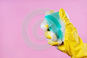 Gloved hand holds a foam sponge on a pink background copy space