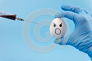 A gloved hand inserts a syringe into a chicken egg close-up on a blue background