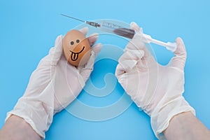 A gloved hand inserts a syringe into a chicken egg close-up on a blue background