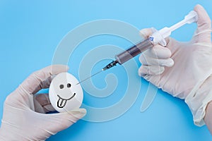 A gloved hand inserts a syringe into a chicken egg close-up on a blue background