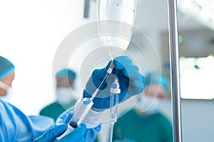 Gloved hand of surgical tech preparing iv fluid bag in operating theatre, with copy space