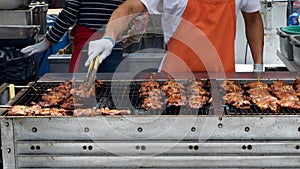 Gloved hand turning meat grilling on large BBQ