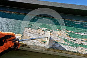 A gloved hand using a scraper to remove old and flaking paint from barge boards, Aotearoa / New Zealand