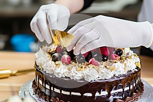gloved hands applying edible gold leaf to a black forest cake