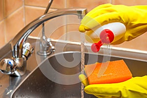 gloved hands with dishwashing liquid and a sponge in the kitchen