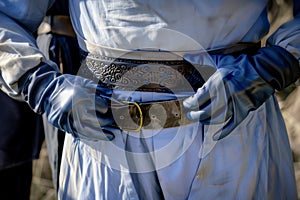 gloved hands fastening a sword belt around waist