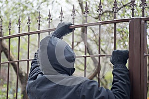 Gloved hands on fence closeup. Male thief an with hands in gloves trying to climb up a metal fence