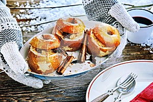 Gloved hands holding a plate of baked apples