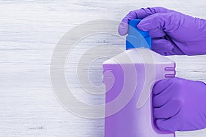 Gloved hands open bottle with cleaning agent on gray background