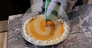Gloved hands pour pumpkin pie filling from a bowl into the pan