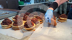 Gloved hands preparing several pulled pork sandwiches