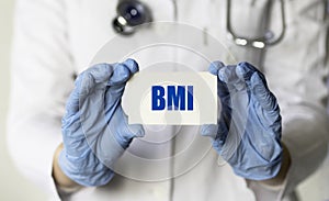 A gloved health worker holds a card with the abbreviation BMI Body Mass Index. Medical concept