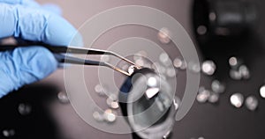 Gloved jeweler holds gem with tweezers and magnifying glass