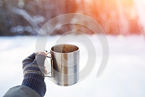 Gloved mitten hand holding a travel mug.