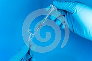 A gloved person uses a syringe to draw a blue liquid from a microcentrifuge tube, probably a reagent. With copy space on a blue