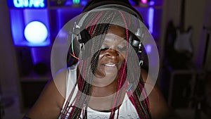 Glowing african american woman streamer in the heart of the gaming room, rocking a night session, stretching arms amidst digital