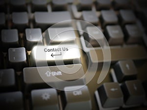 A glowing bright `contact us` button, key, message on the keyboard. Customer service concept. Internet or online contact for