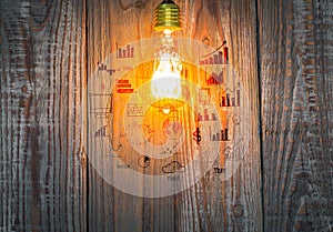 Glowing bulb with drawing graph on the wood