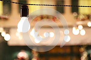 Glowing bulb on wire against lights. Space for text