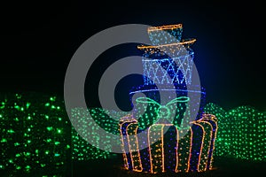 Glowing cake object in the dark.Multitiered cake made of green, blue and purple garlands in the dark.Installation with