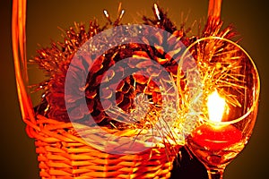 Glowing Christmas composition with goblet candle light and pine cones in a wicker basket on a dark background