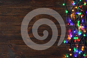 Glowing Christmas lights on brown wooden background, top view