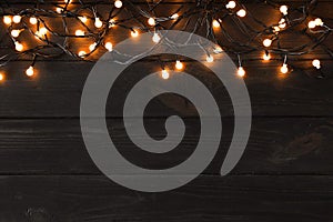 Glowing Christmas lights  dark wooden background, top view. Space for text