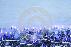 Glowing Christmas lights and fir branches on wooden background