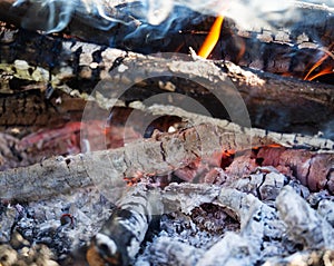 Glowing embers in the ash with log in smoke, closeup