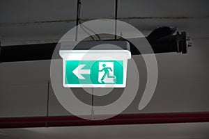 Glowing Emergency exit sign with left arrow at a building. Safety first concept. Copy space wallpaper. Exit signs with light in a
