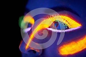 Glowing eyes. A young woman with with neon paint on her face posing.