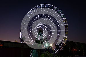 A glowing Ferris wheel against the night sky. Tourist attraction for children and adults, holiday and travel concept