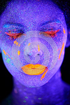 Glowing goddess in the dark. a young woman posing with neon paint on her face.