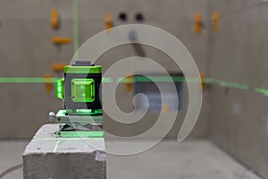 Glowing green laser spirit level built on a brick at a construction site with green lines. Accurate measurement of construction