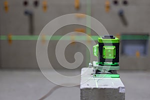 Glowing green laser spirit level built on a brick at a construction site with green lines. Accurate measurement of construction in