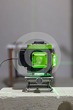 Glowing green laser spirit level built on a brick at a construction site with green lines. Accurate measurement of construction