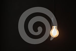 Glowing light bulb hanging on dark background. Space for text