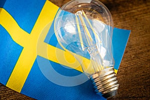 A glowing light bulb lying in the middle of the Swedish flag, Concept, Energy prices in Sweden