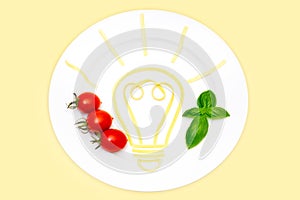 Glowing light bulb made from boiled pasta, cherry tomatoes and basil on a white plated isolated on yellow