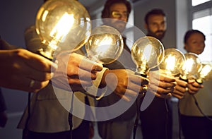 Glowing light bulbs in hands of creative business team in office as symbols of their ideas.