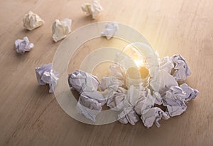 Glowing lightbulb with crumpled paper ball on wooden table.