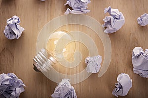 Glowing lightbulb with crumpled paper ball on wooden table.