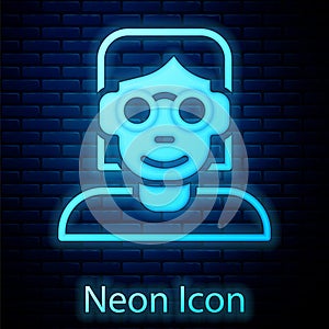 Glowing neon Hacker or coder icon isolated on brick wall background. Programmer developer working on code, coding