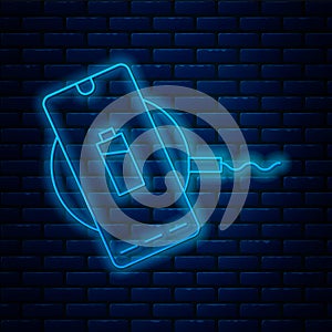 Glowing neon line Smartphone charging on wireless charger icon isolated on brick wall background. Charging battery on