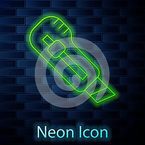 Glowing neon line Stationery knife icon isolated on brick wall background. Office paper cutter. Vector