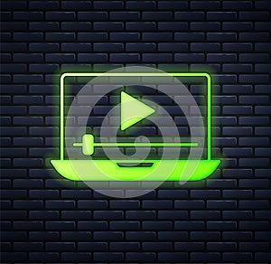 Glowing neon Online play video icon isolated on brick wall background. Laptop and film strip with play sign. Vector