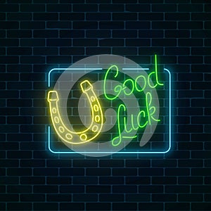 Glowing neon sign with good luck wish and horseshoe in rectangle frame on dark brick wall background.